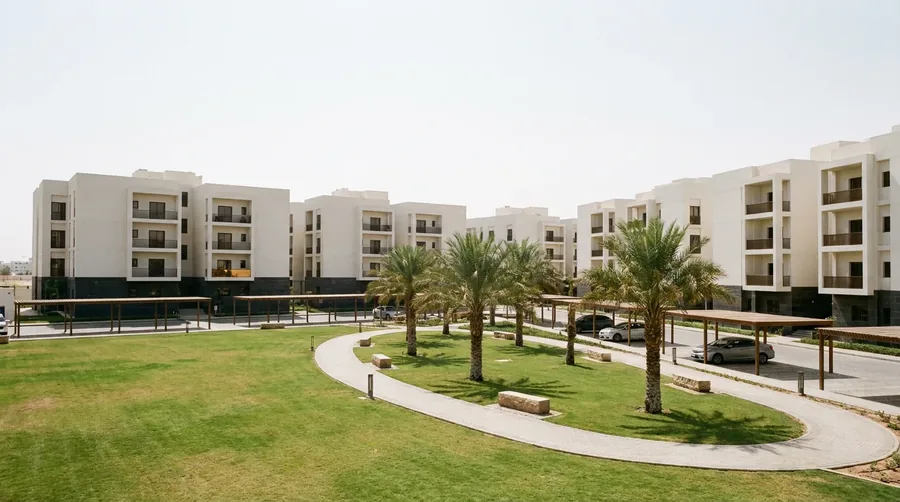 Four-storey white apartment buildings with basalt-banded bases arranged around a shared green and a paved walking loop.
